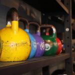 A picture of different types of colored kettlebells from the side of a storage rack