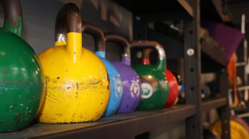 A picture of different types of colored kettlebells from the side of a storage rack