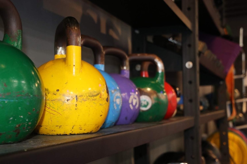 A picture of different types of colored kettlebells from the side of a storage rack